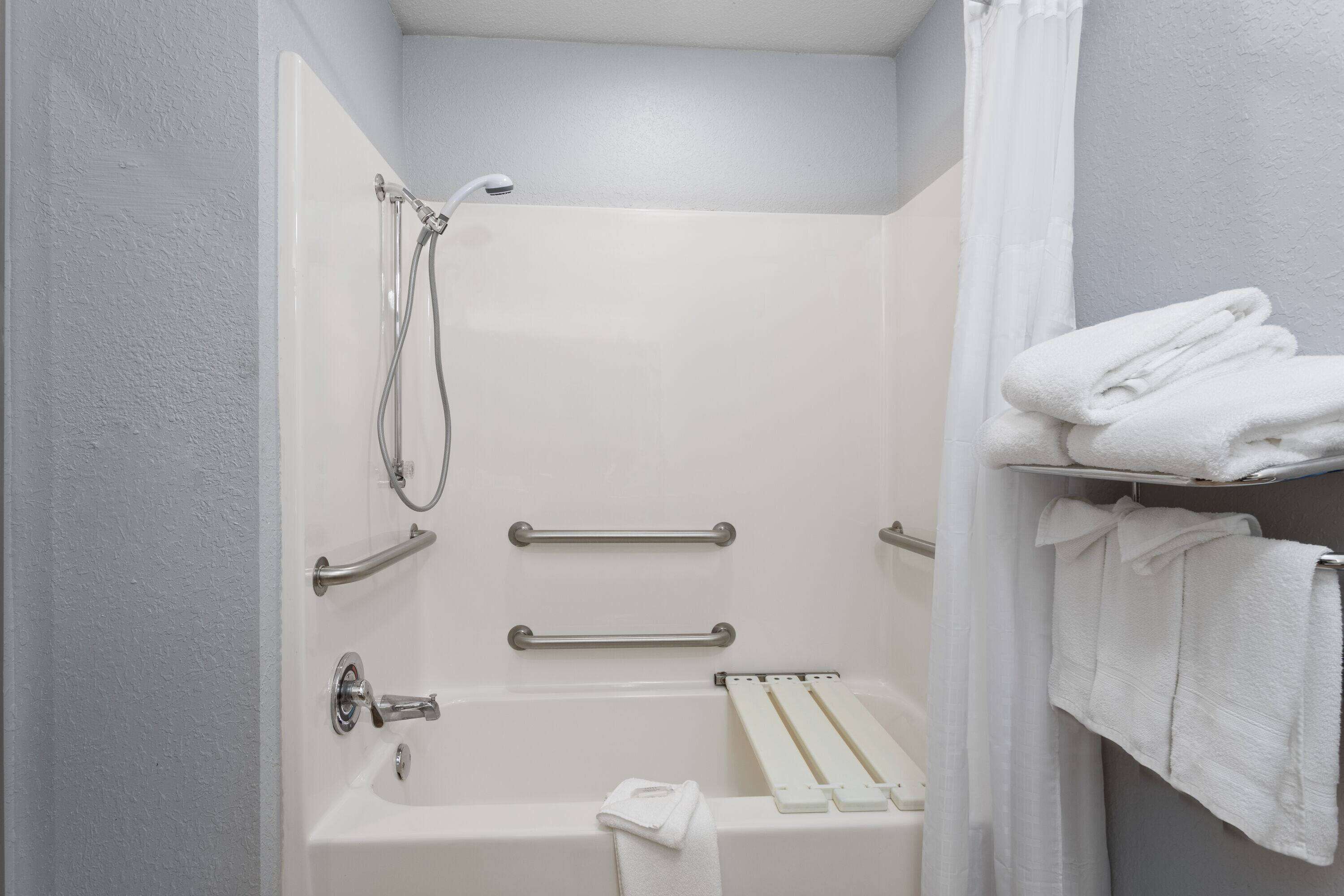 A bathroom with a bathtub, grab bars, a showerhead, and a towel rack with towels.