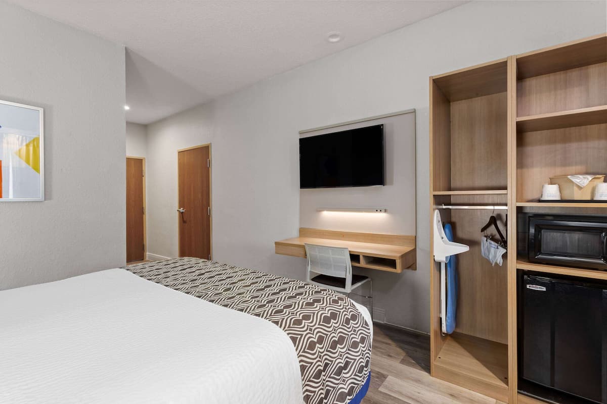 Una habitación de hotel con cama, escritorio con silla, televisor y armario.