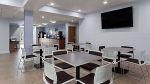 A dining area with tables and chairs, a kitchen in the background, and a flat-screen TV mounted on the wall. - Microtel Inn & Suites by Wyndham Zephyrhills (Zephyrhills)