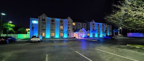 Un hôtel à plusieurs étages, doté d’un design moderne, comprenant un parking et plusieurs voitures garées devant.