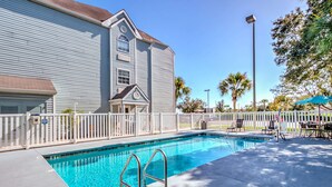 A swimming pool with a white fence, a building with a gabled roof, and palm trees in the background. - Microtel Inn & Suites by Wyndham Zephyrhills (Zephyrhills)
