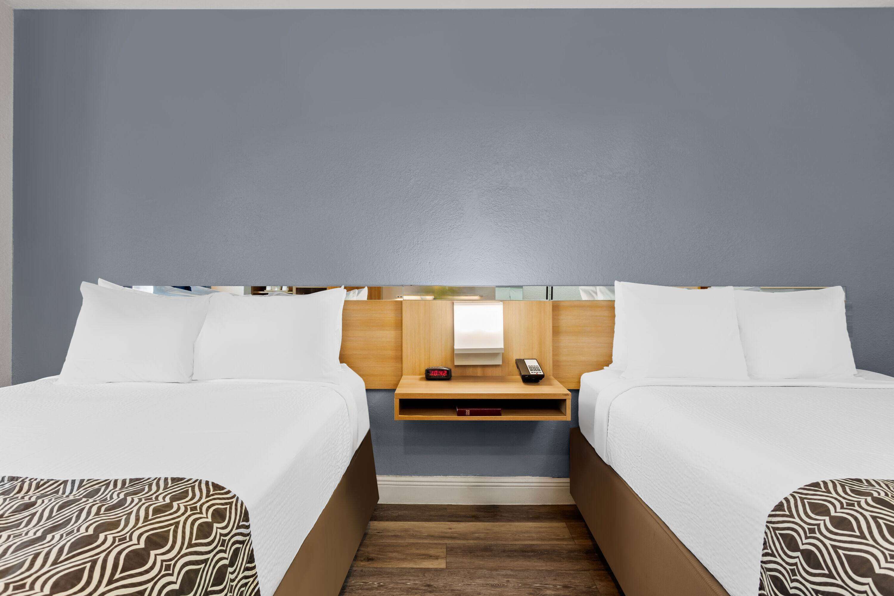 A hotel room with two beds, a wooden nightstand, a small table, and a mirror.