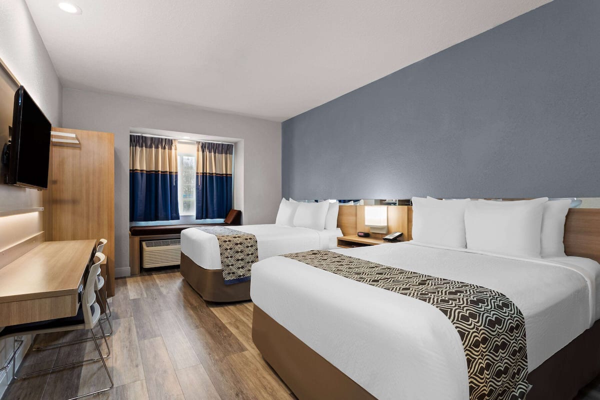 Una habitación de hotel con dos camas, un escritorio, una silla, un televisor y una ventana con cortinas.