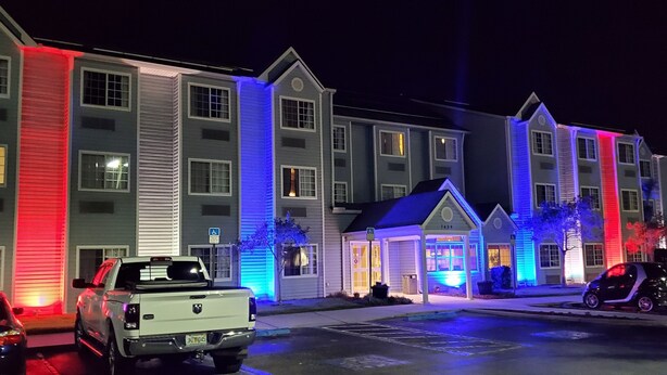 A multi-story hotel with a parking lot and a small building with a sign. - Microtel Inn & Suites by Wyndham Zephyrhills (Zephyrhills)