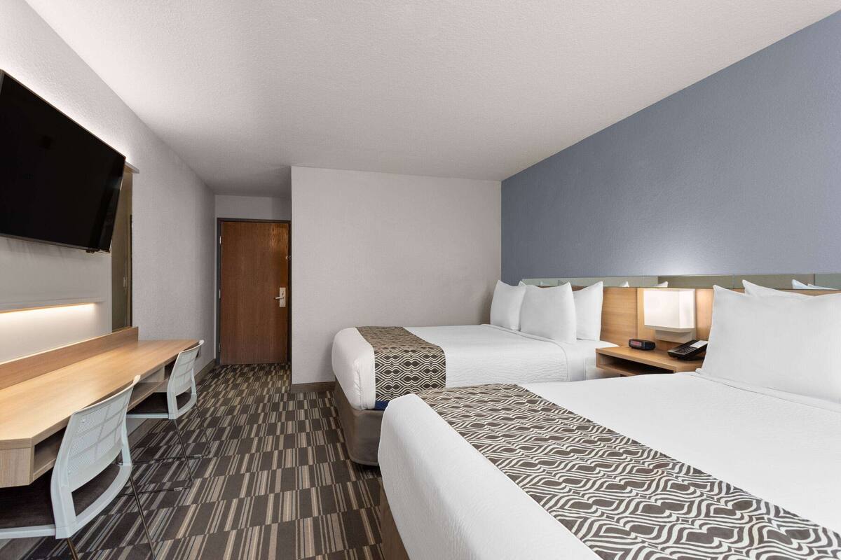 Habitación de hotel con un escritorio de madera, dos camas, un televisor de pantalla plana y una colcha estampada.