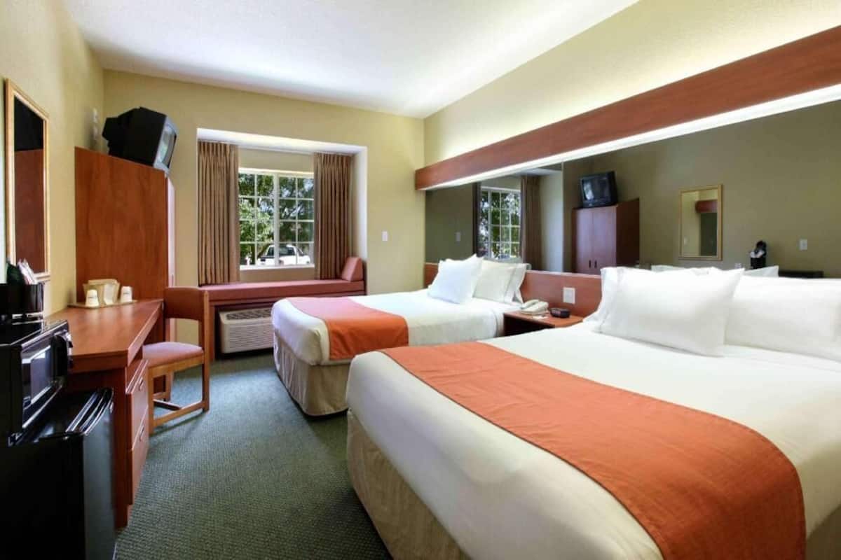 Habitación de hotel con dos camas, un escritorio, una silla, un televisor y una ventana con cortinas.