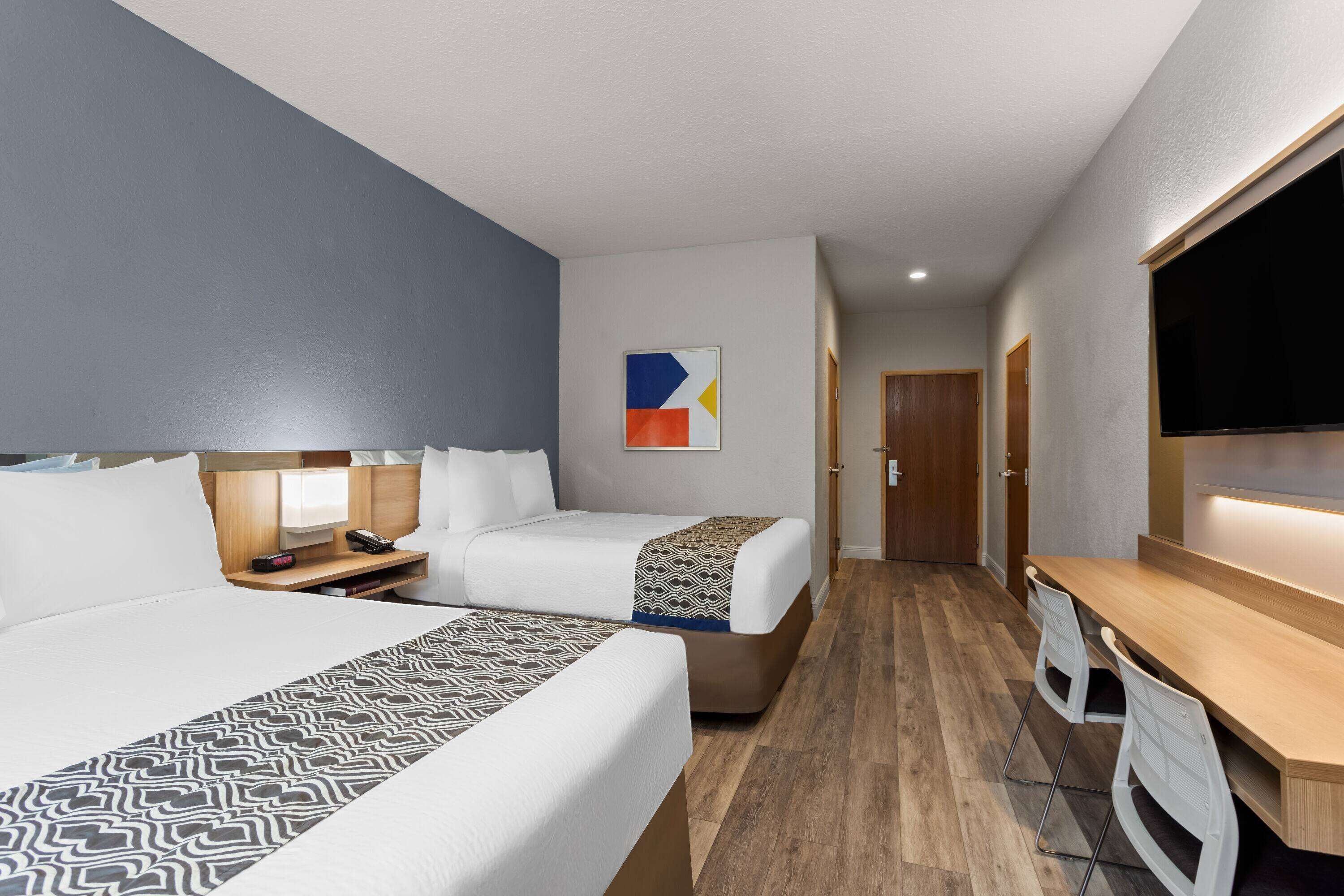 Habitación de hotel con dos camas, un escritorio, una silla, un televisor y una puerta que da a otra habitación.