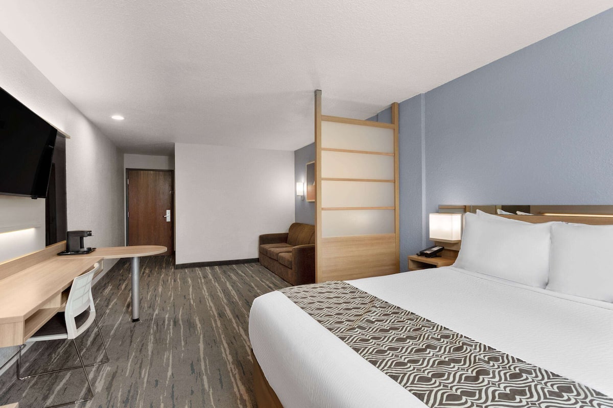 Una habitación de hotel con cama, escritorio, silla, armario y televisor.