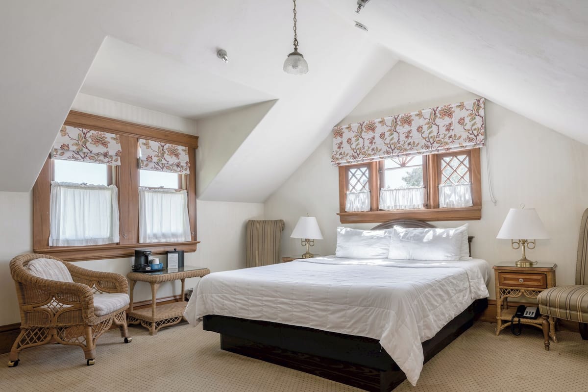 A bedroom with a bed, two bedside tables, a chair, a window with curtains, and a hanging light fixture.