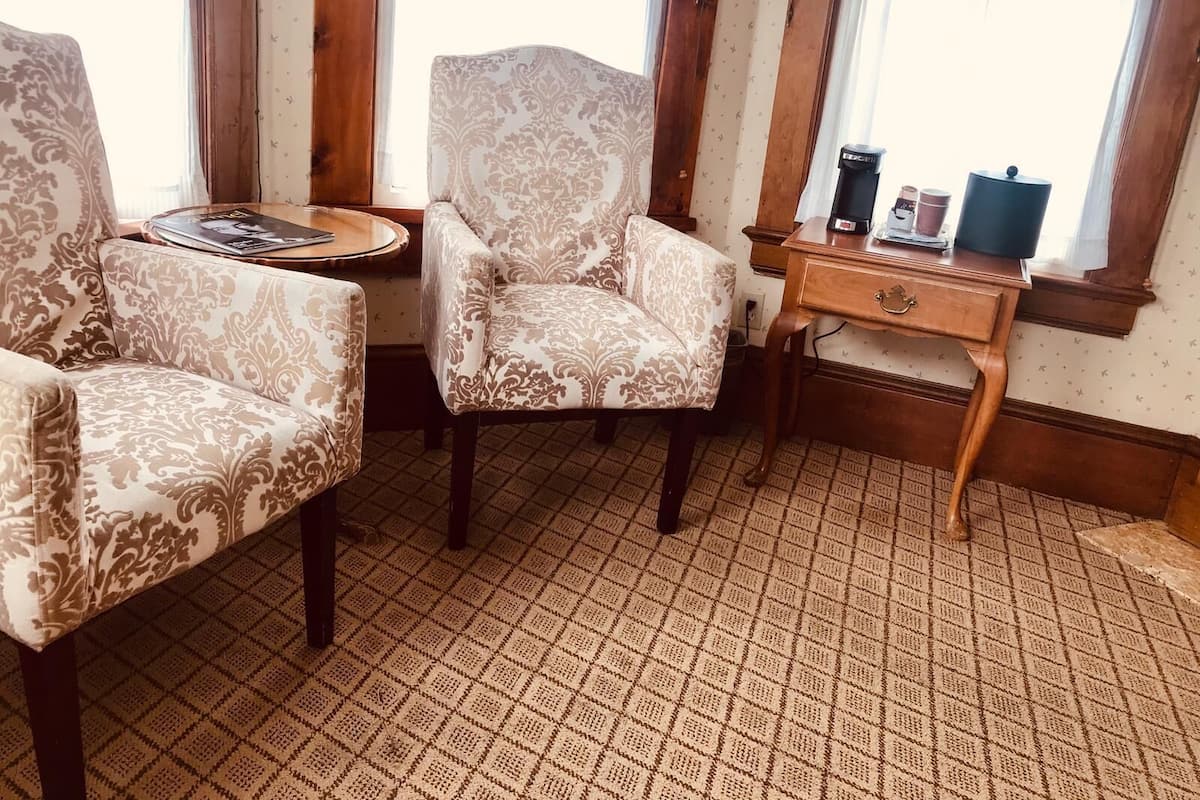 A room with patterned armchairs, a small wooden table with a magazine, and a desk with a coffee maker.