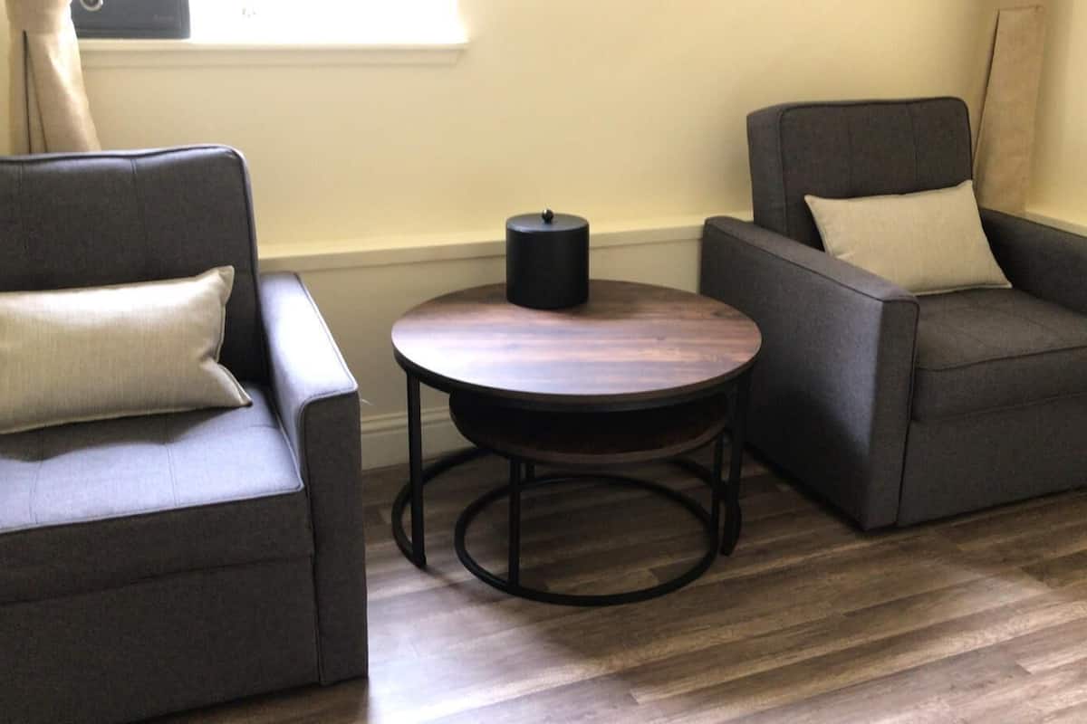 A room with two grey armchairs, a round wooden table, and a black cylindrical object on the table.