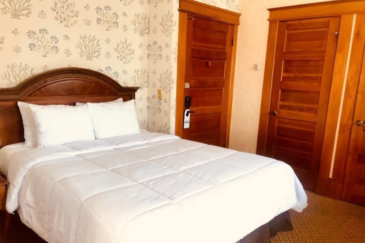 A neatly made bed with white bedding in a room with floral wallpaper and wooden doors.