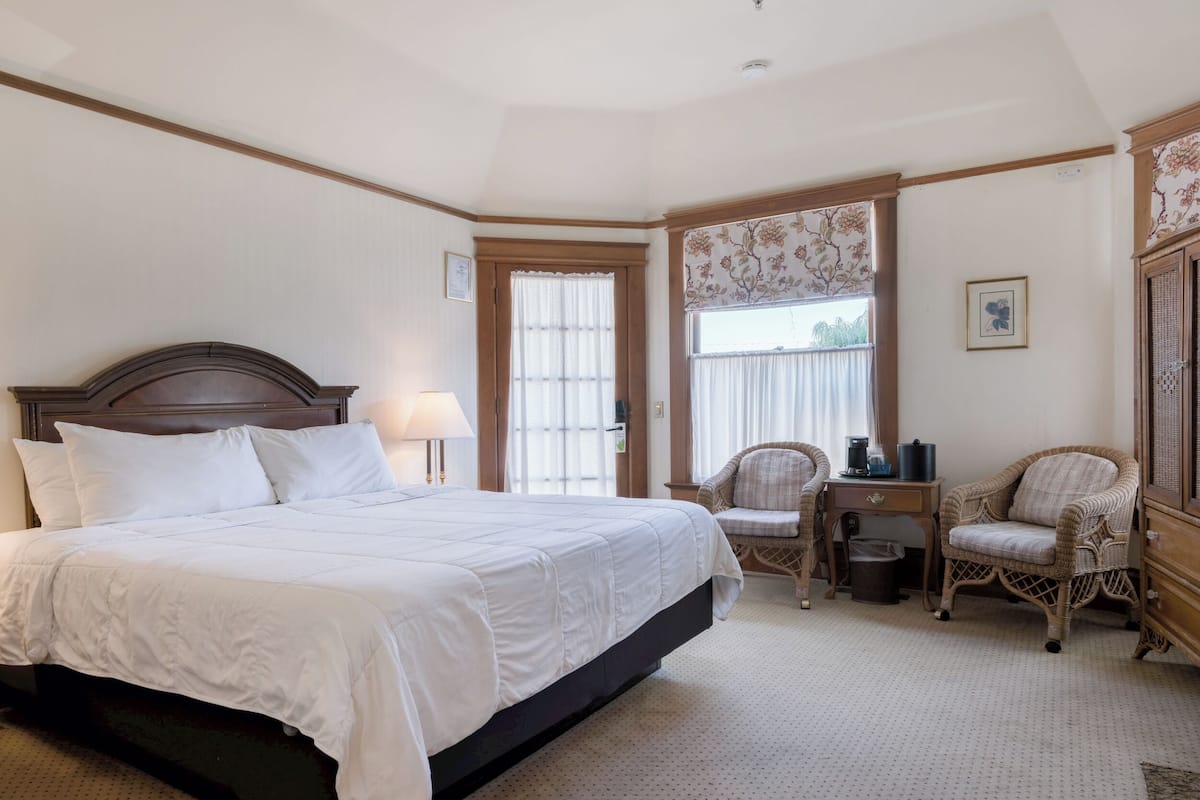 A bedroom with a large bed, a desk, a chair, and a window with curtains.