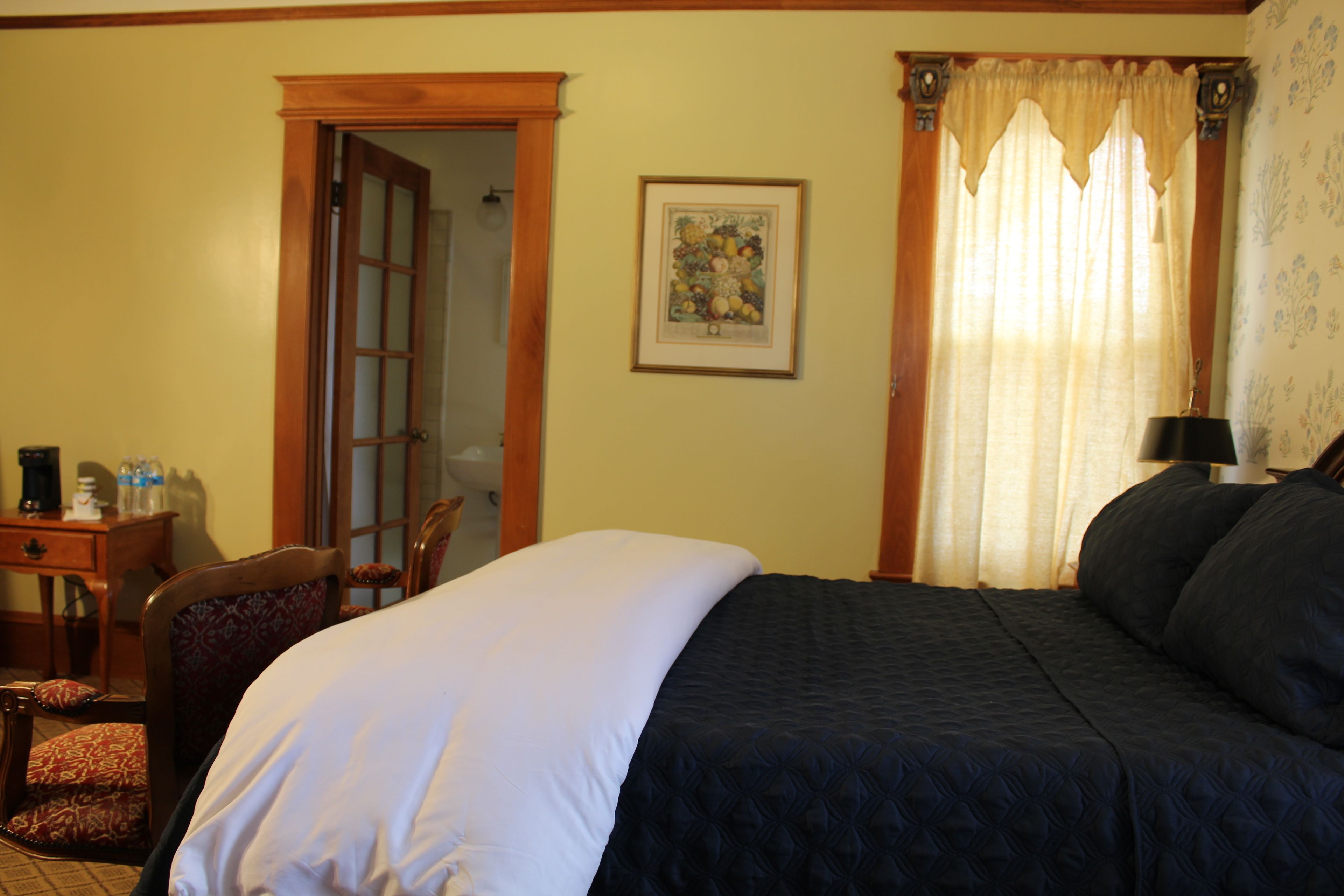 Une chambre d’hôtel avec un grand lit, une chaise, un bureau avec une lampe et un tableau encadré au mur.