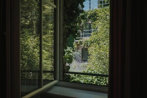 Ένα παράθυρο με θέα σε έναν κήπο και ένα κτίριο.