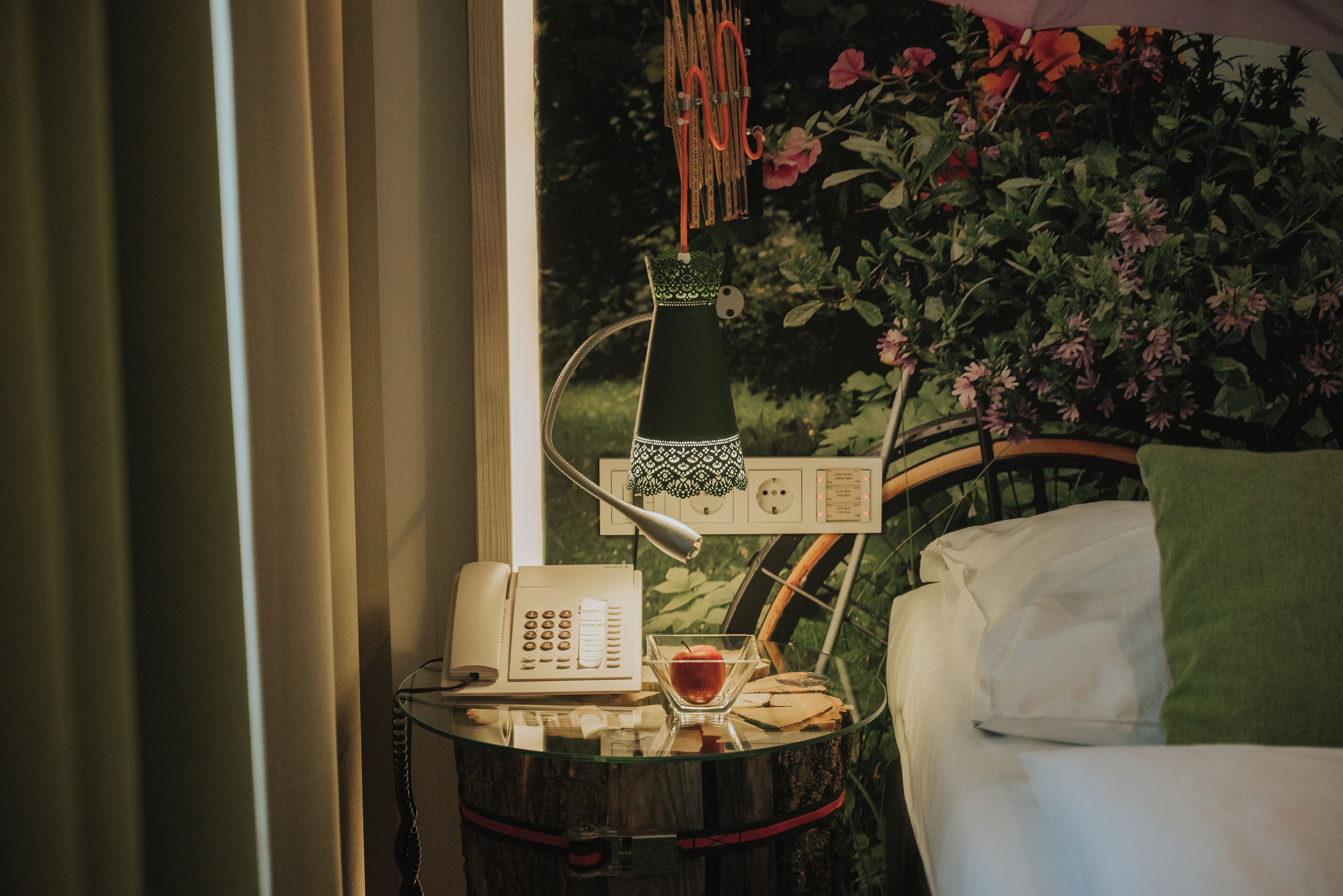 A room with a bed, a bedside table with a lamp, a phone, and a bowl with an apple.