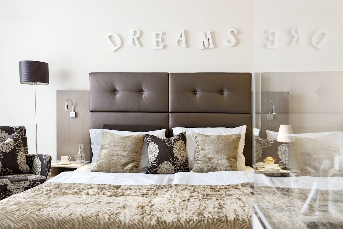 A neatly arranged bedroom with a large bed, a bedside table with a lamp, and a chair.
