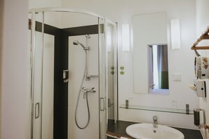 Ένα σύγχρονο μπάνιο με ένα ντους που διαχωρίζεται με γυάλινο διάφραγμα, έναν λευκό νιπτήρα και έναν καθρέφτη πάνω από τον νιπτήρα.