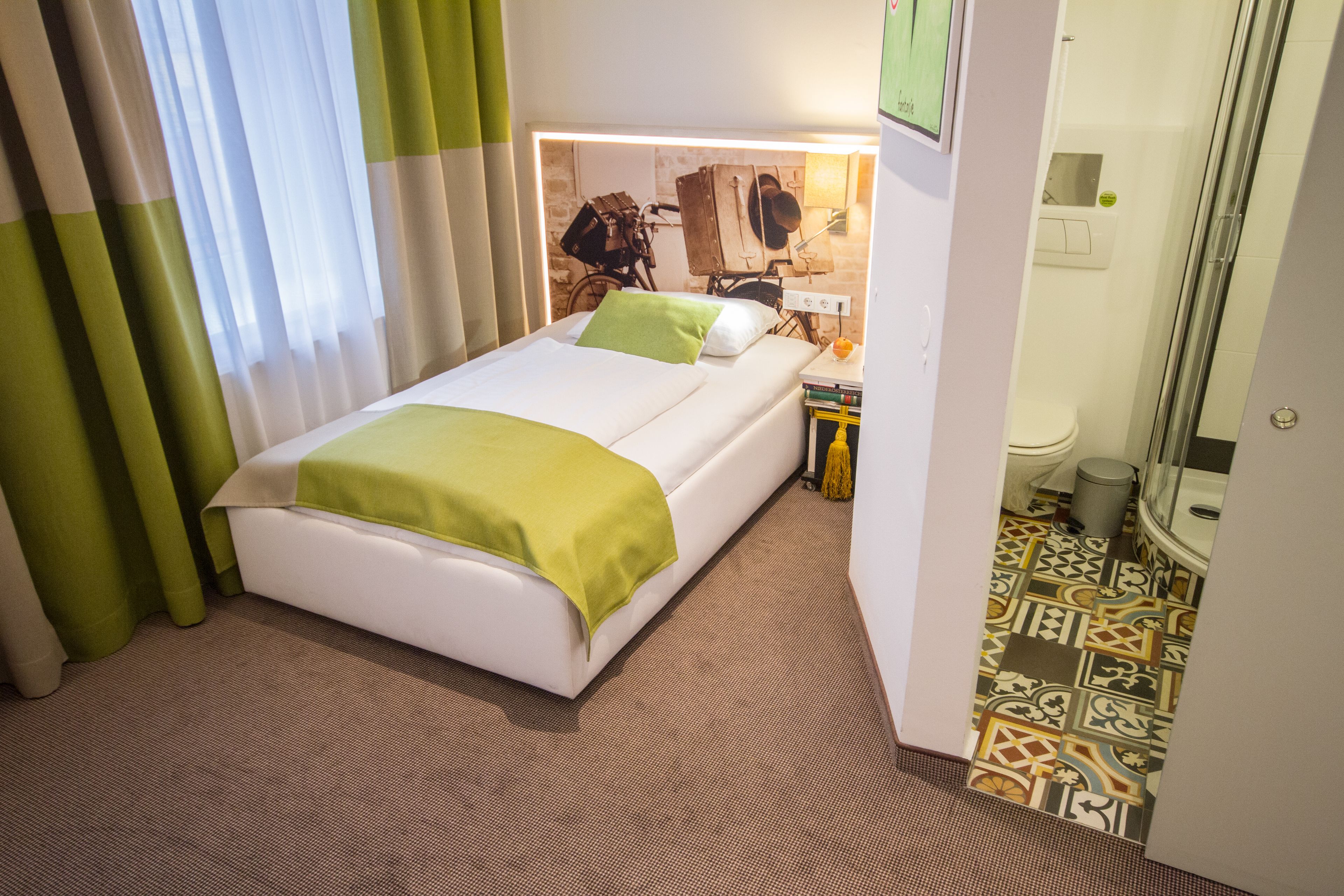Una habitación de hotel con cama, una mesita de noche, un espejo y zona de ducha.