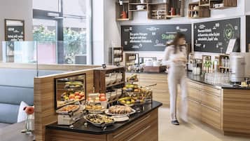 Zona de desayuno de hotel con sistema de buffet, muebles de madera y un ventanal con vistas al exterior.