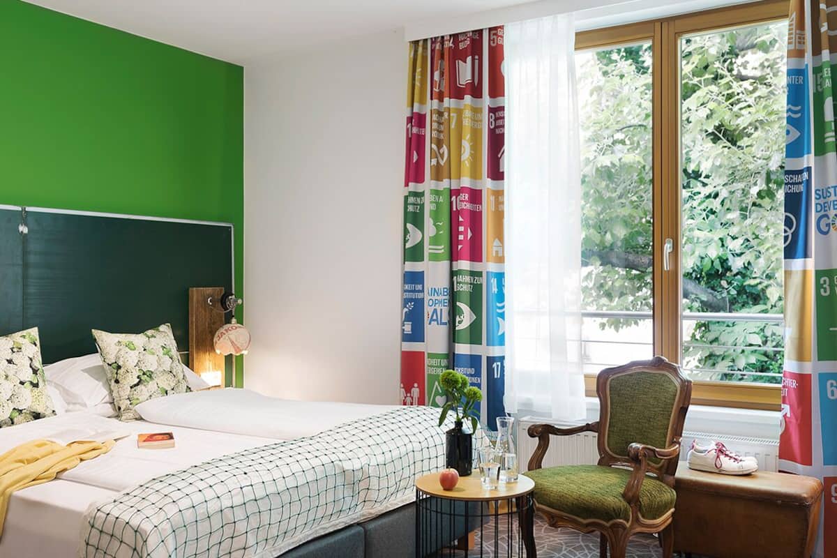 A hotel room with a bed, a chair, a small table, and a window with curtains.