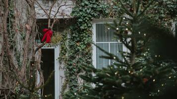Un edificio con muros cubiertos de hiedra y una ventana decorada con un lazo rojo.