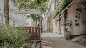 Una estrecha calle urbana flanqueada por edificios, una cerca de madera y un toldo blanco.