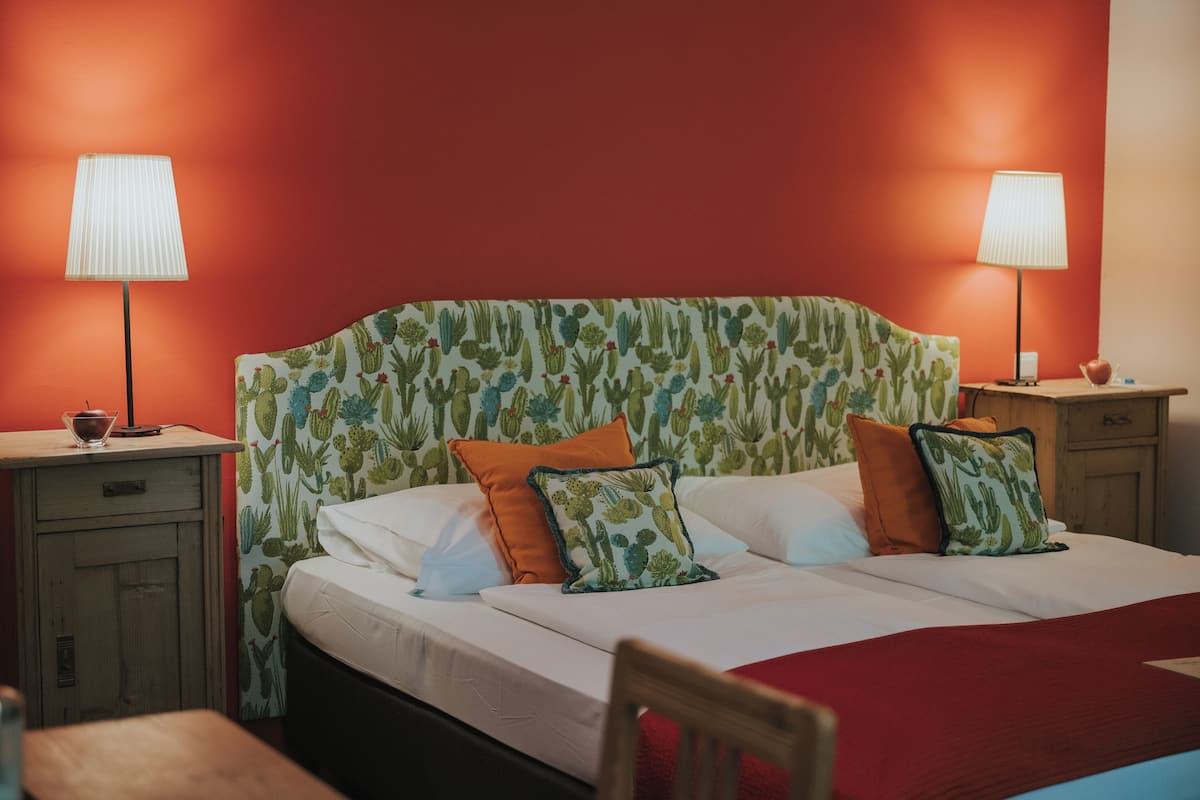 A bed with a cactus-patterned headboard, two bedside lamps, and a wooden nightstand with a cup and saucer.