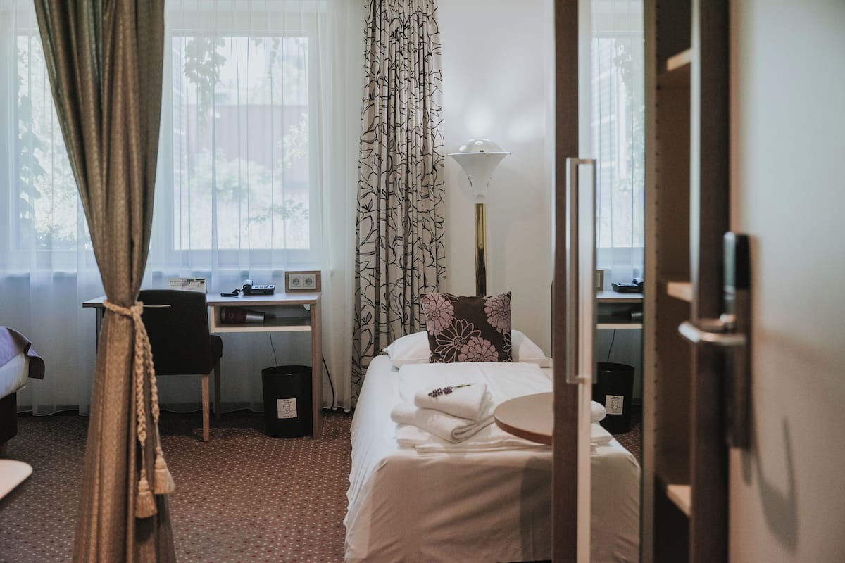 A hotel room with a bed, a desk, a chair, a lamp, and a window with curtains.