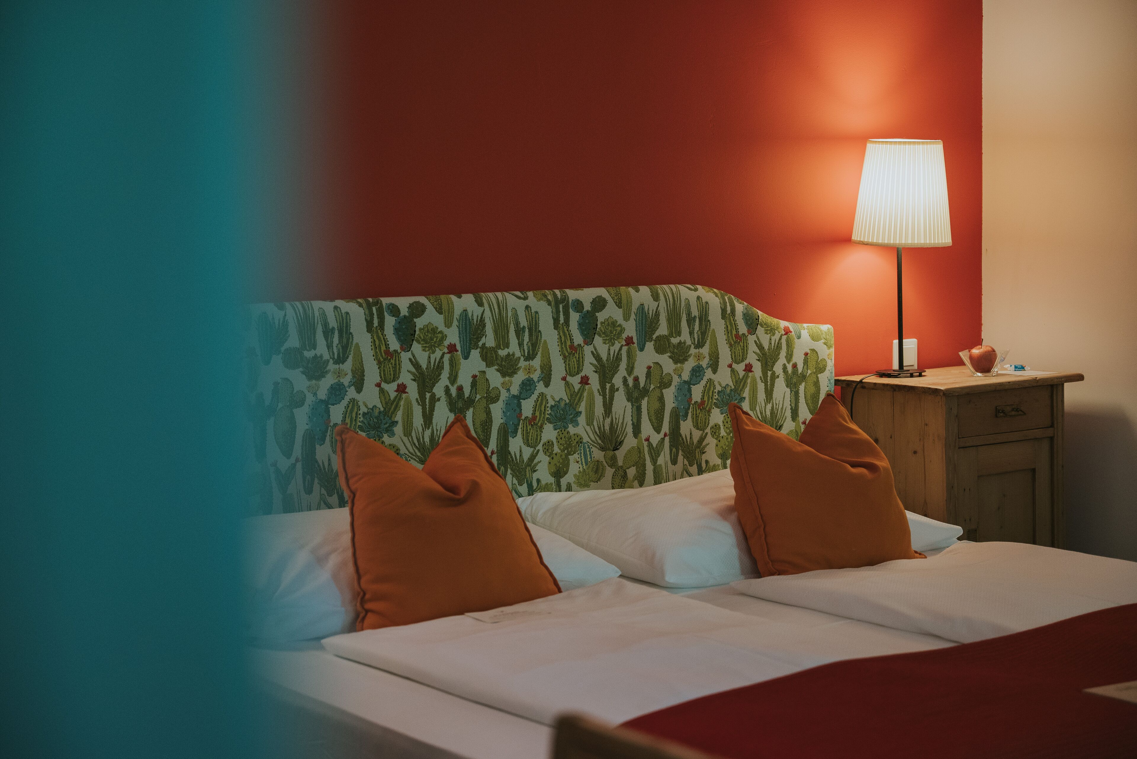 A hotel room with a bed, pillows, a nightstand, and a lamp.