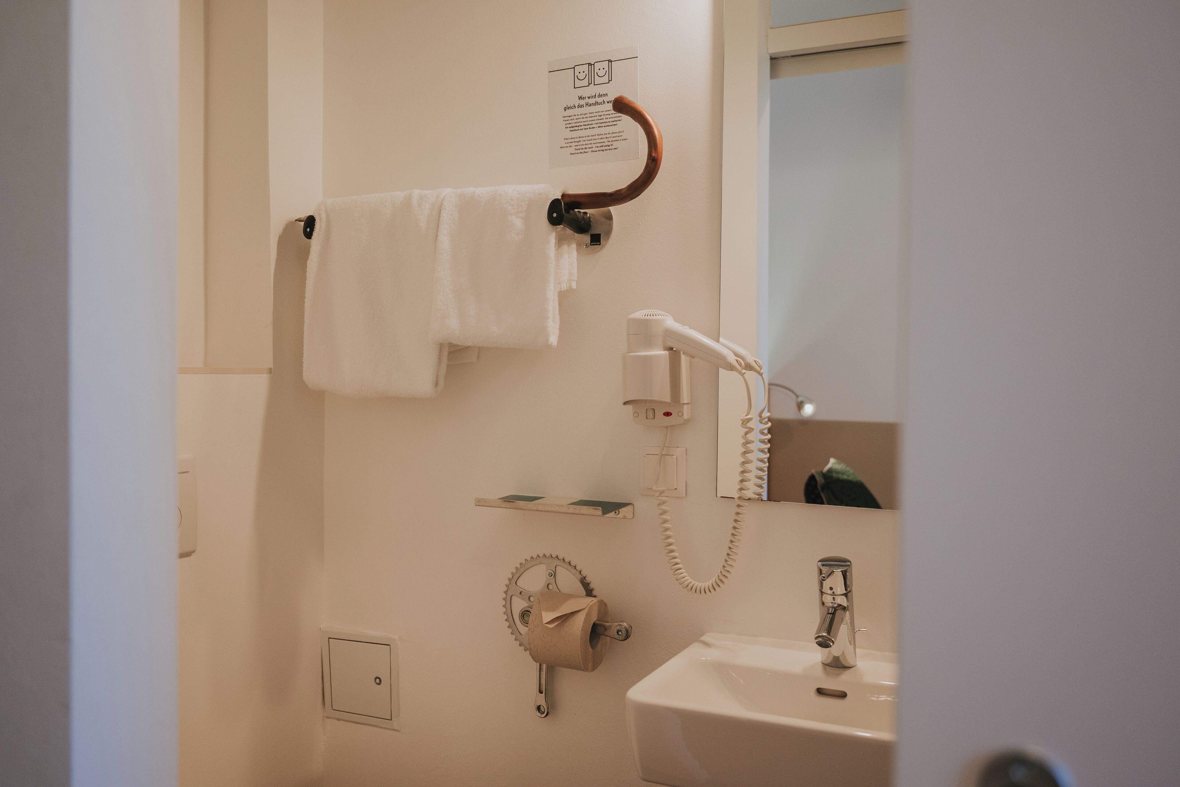 Un baño con toallero, secador de pelo, dispensador de papel higiénico, lavamanos y espejo.