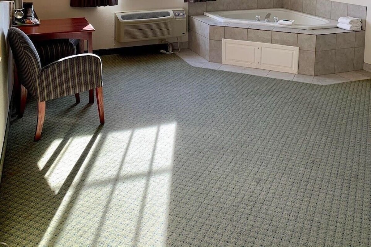 A hotel room with a large window, a sitting area with a table and chair, a bathtub, and a radiator.