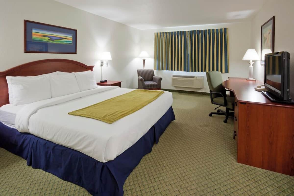 A hotel room with a large bed, a desk with a television, a chair, a desk lamp, and a window with curtains.