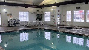 A swimming pool with clear water, surrounded by white chairs and a small table.