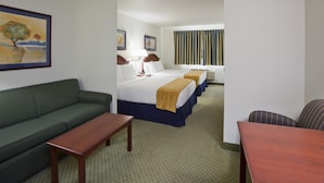 A hotel room with a green sofa, a wooden table, two beds with blue and white bedding, and a window with striped curtains.