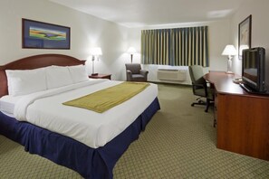 A hotel room with a large bed, a desk, a chair, a television, and a window with striped curtains.