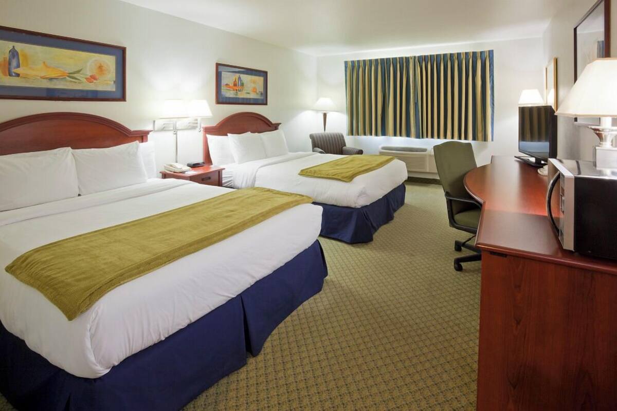 A hotel room with two beds, a desk, a chair, and a television.