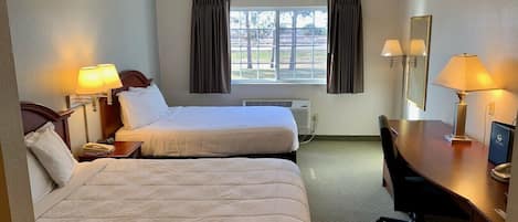 A hotel room with two beds, a desk, a chair, a window with curtains, and a mirror.