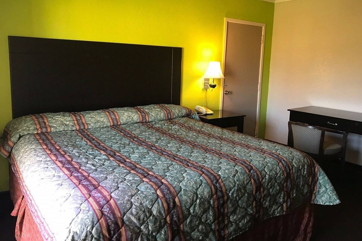 A hotel room with a large bed, a bedside table with a lamp, and a door.