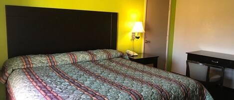 Una habitación de hotel con una cama grande, una mesita de noche con lámpara y una puerta.