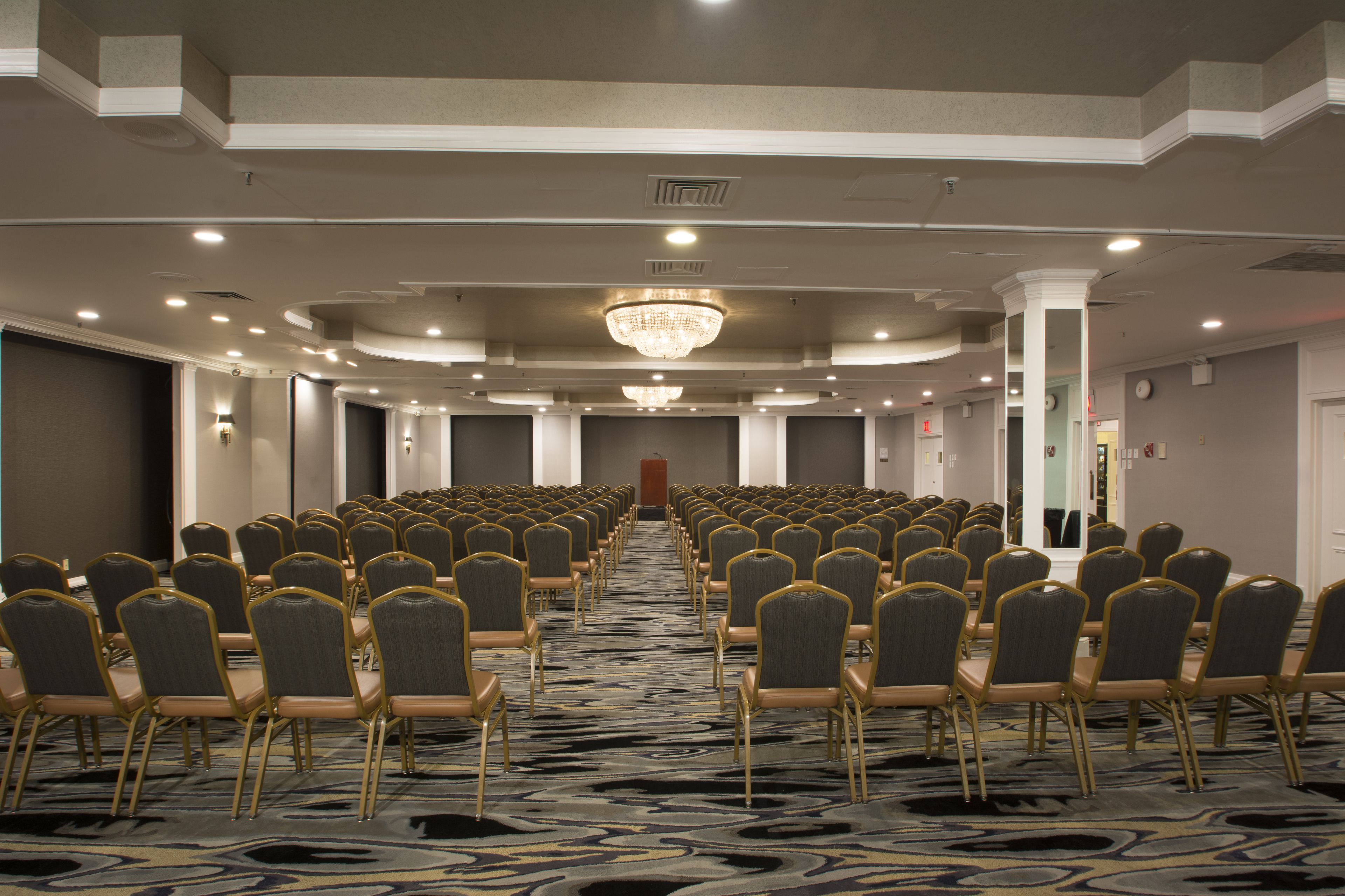 A conference room with rows of chairs, a chandelier, and a carpeted floor.