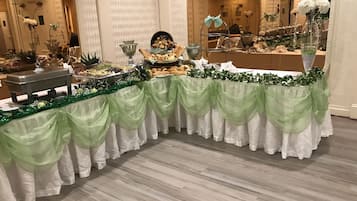 A buffet table with a green and white draped tablecloth, various food items, and decorative greenery.