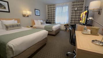 A hotel room with two beds, a desk, a chair, a television, and a window with curtains.