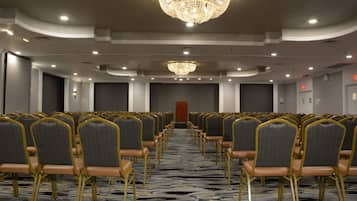 A conference room with rows of chairs, a chandelier, and a carpeted floor.
