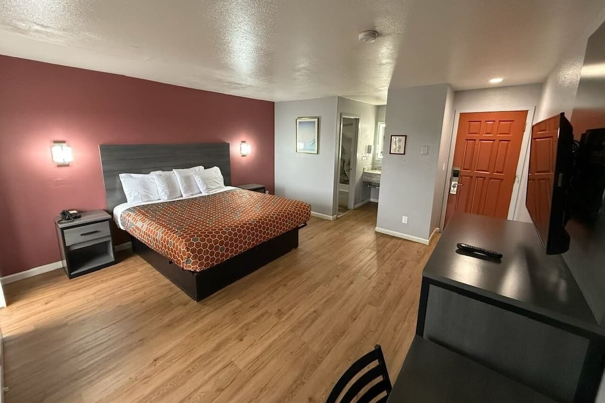 A hotel room with a bed, bedside table, and a desk with a chair.
