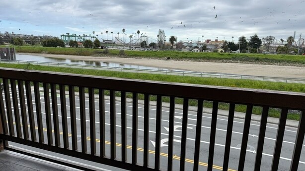 A view from a balcony with a metal railing overlooking a road with a water body and distant buildings. - Ocean Gate Inn (Santa Cruz)
