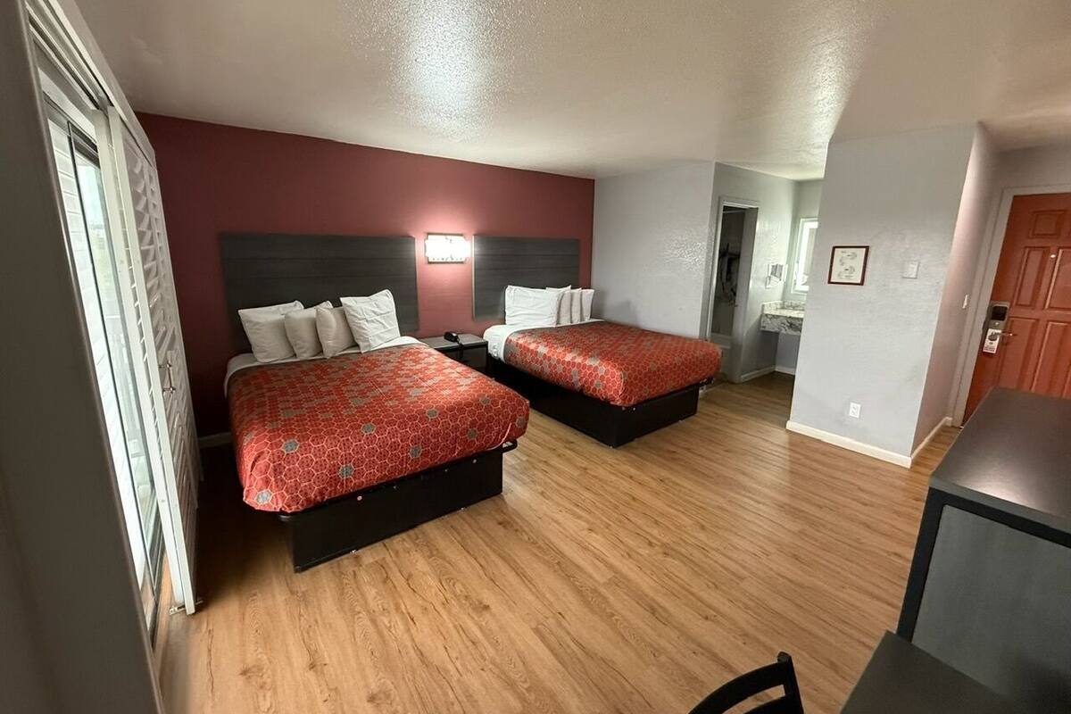 A hotel room with two beds, a desk, and a kitchenette.