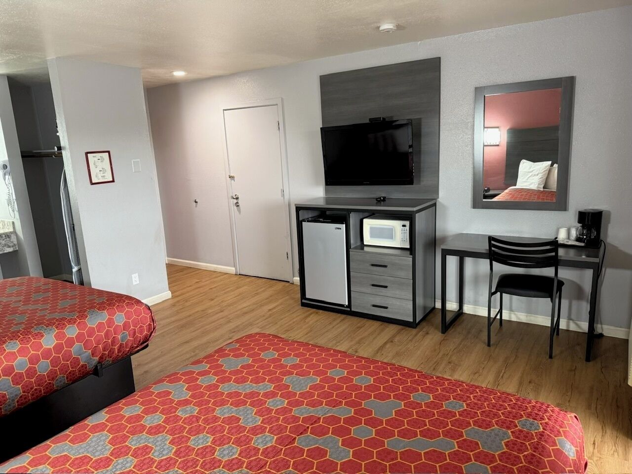 A hotel room with two beds, a TV, a small kitchenette, and a desk with a chair.