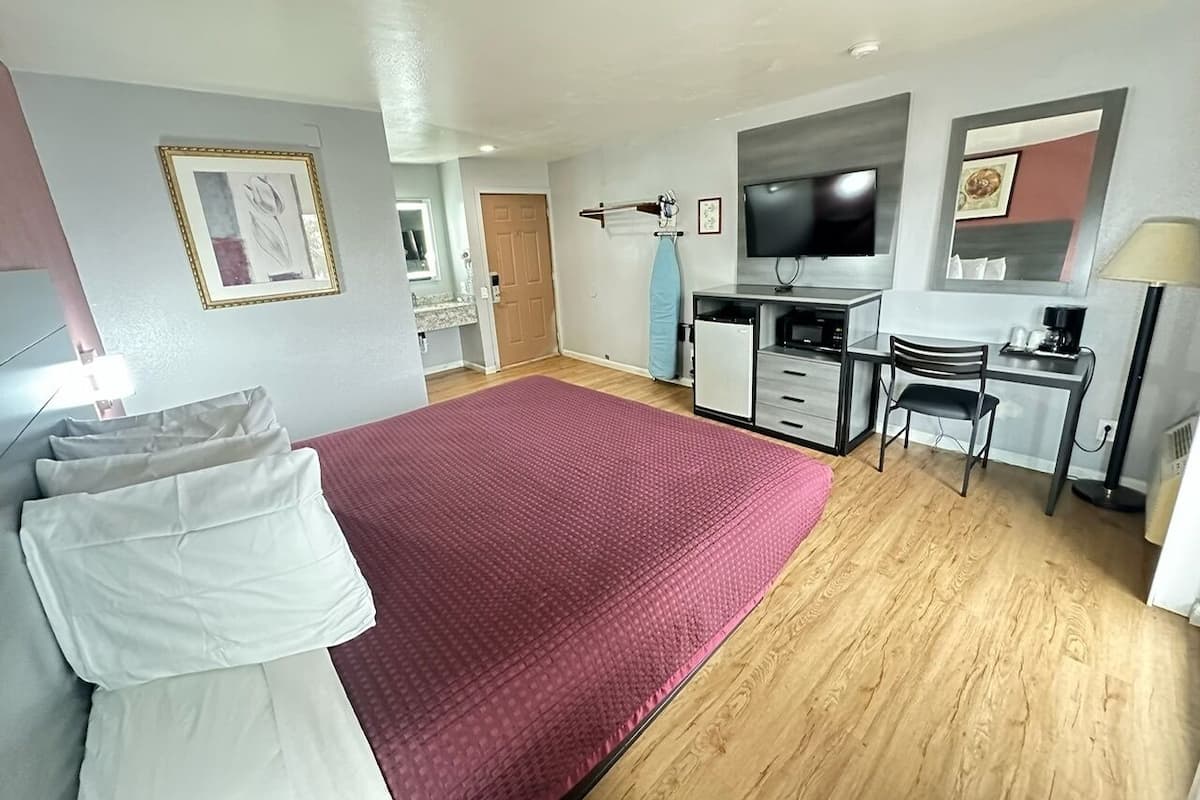 A hotel room with a large bed, a desk with a chair, a television, and a small kitchenette.