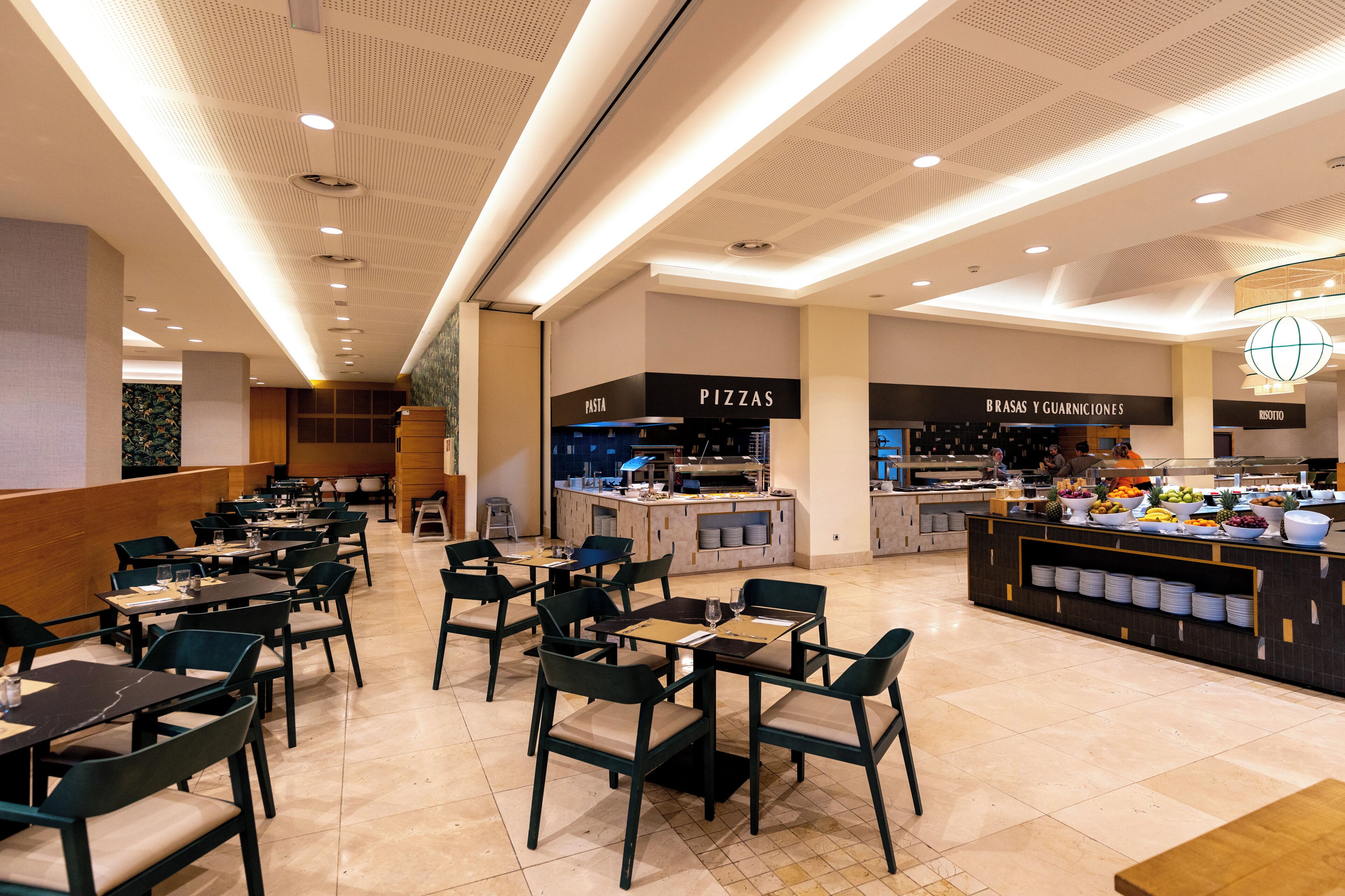A modern restaurant with multiple dining areas, a central counter with a variety of food items, and clearly labeled sections for pizzas and other dishes.